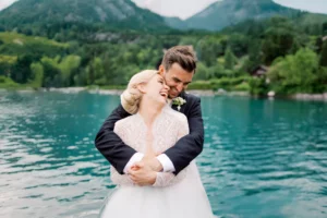 A happy bride and groom embrace by a turquoise lake, captured by a wedding photographer Geneva.
