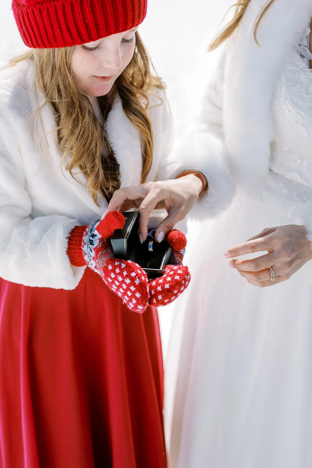 Close-up of a girl in red mittens holding an open ring box during a winter wedding session in Chamonix.
