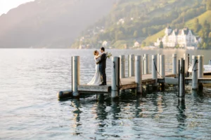 A bride and groom embrace on a wooden pier on a lake in Switzerland, with majestic mountains in the background, a moment captured by their wedding photographer in Switzerland.