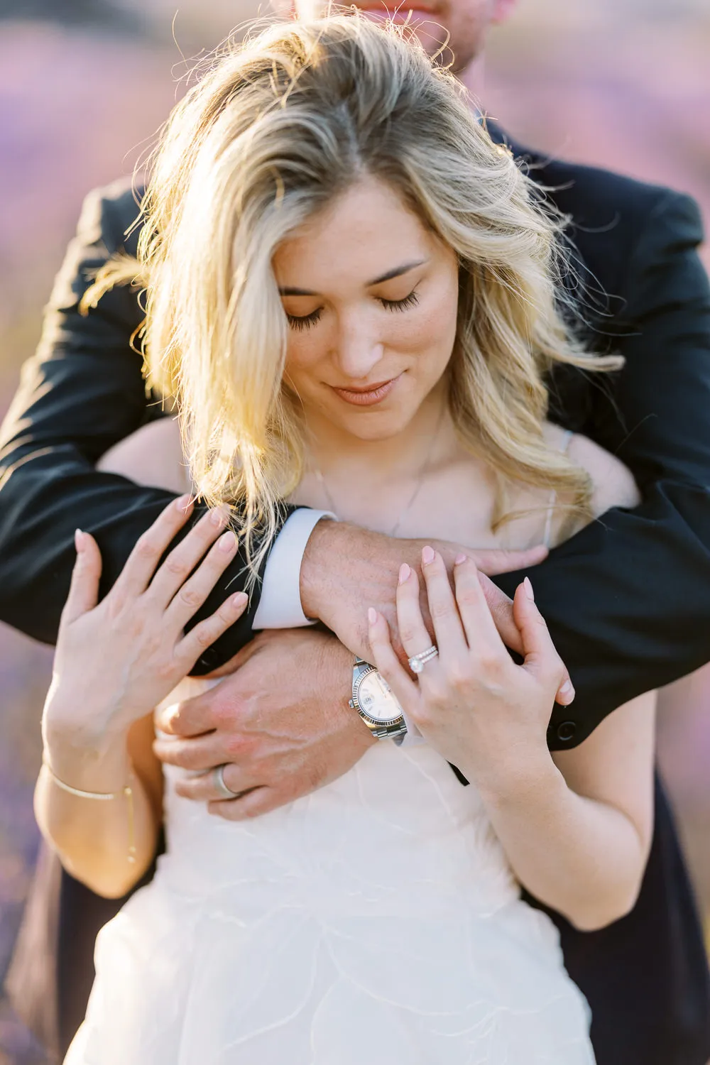 A close-up detail shot of a bride’s hands and engagement ring, held gently by her groom as he embraces her. Photo by a wedding photographer in Provence.