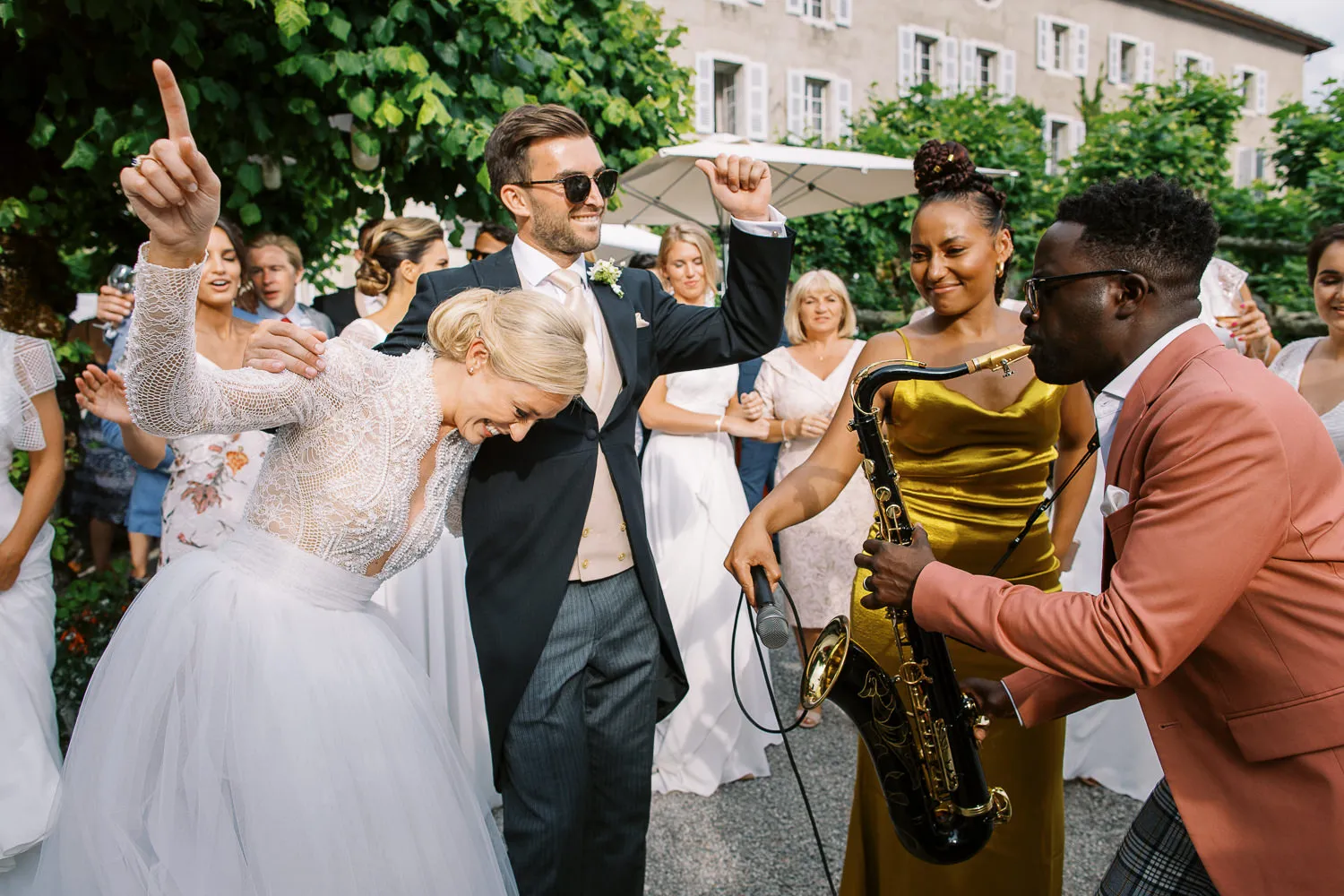 Bride and groom laughing and dancing outdoors with guests and a live saxophone player at a Provence wedding - captured by wedding photographer Provence.