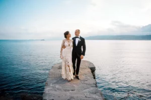 An elegant bride and groom walk on a stone pier overlooking the Mediterranean Sea, a romantic moment captured by their wedding photographer in Malta.