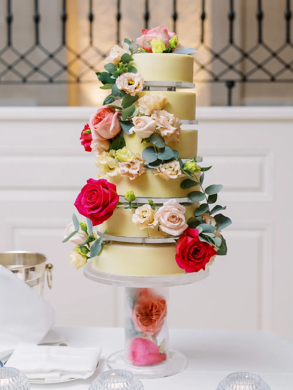 Elegant multi-tiered yellow wedding cake adorned with fresh pink and red roses - detail by wedding photographer French Riviera.