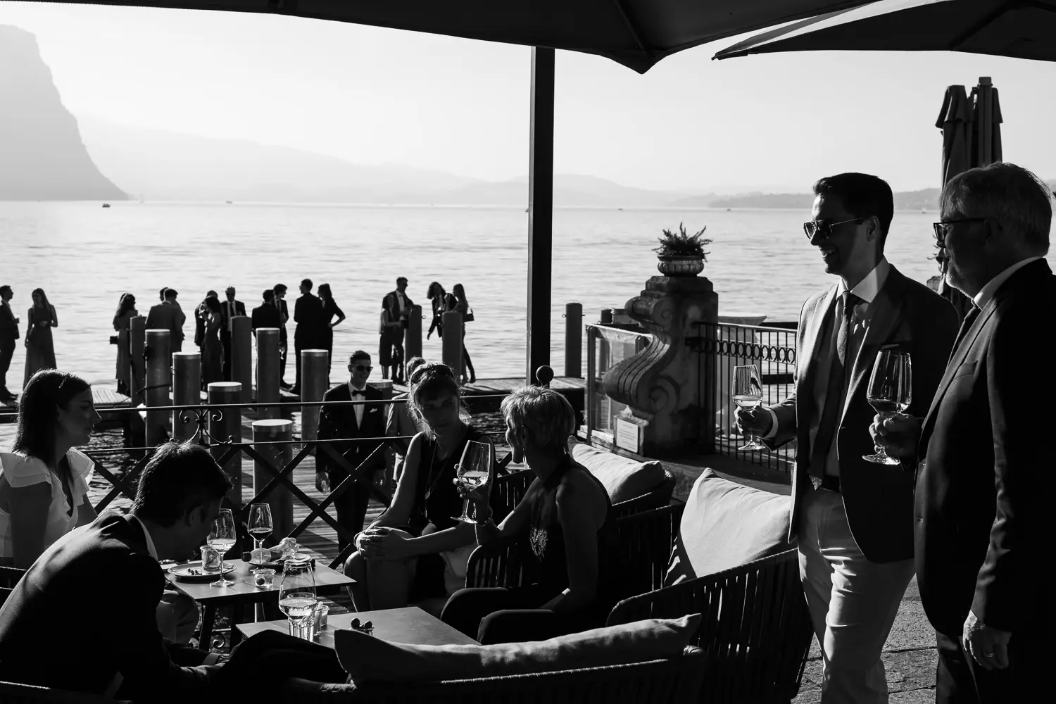 Black and white photo of wedding guests mingling and chatting on a terrace overlooking Lake Geneva - atmosphere captured by wedding photographer Geneva.