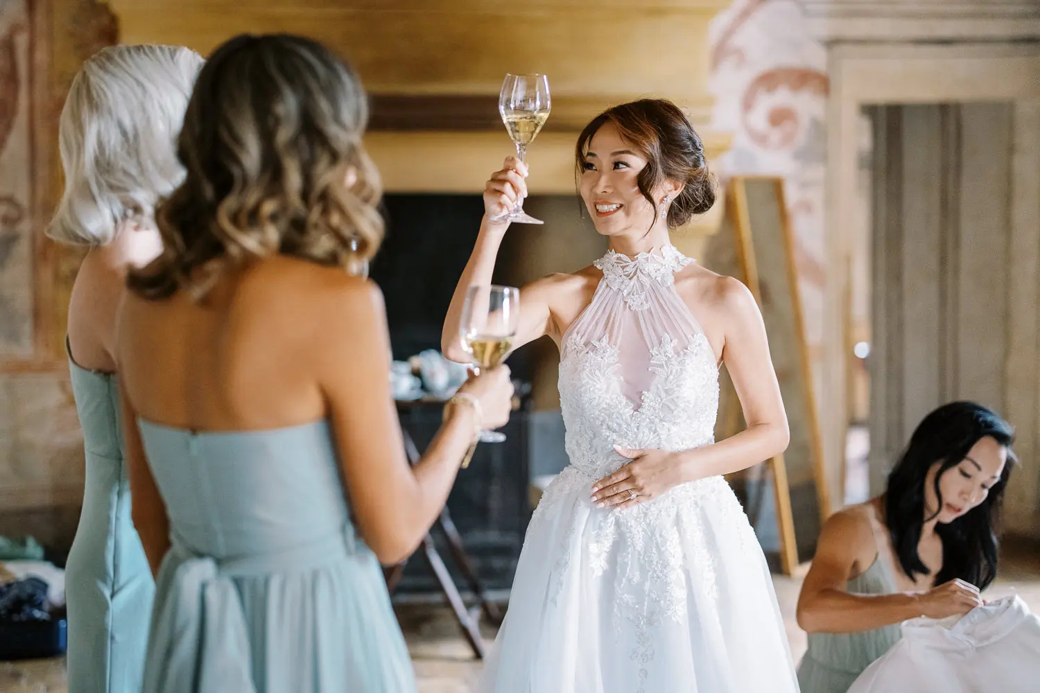 Smiling bride in intricate gown toasting champagne with bridesmaids before her Geneva wedding - wedding photographer Geneva capturing pre-wedding moments.