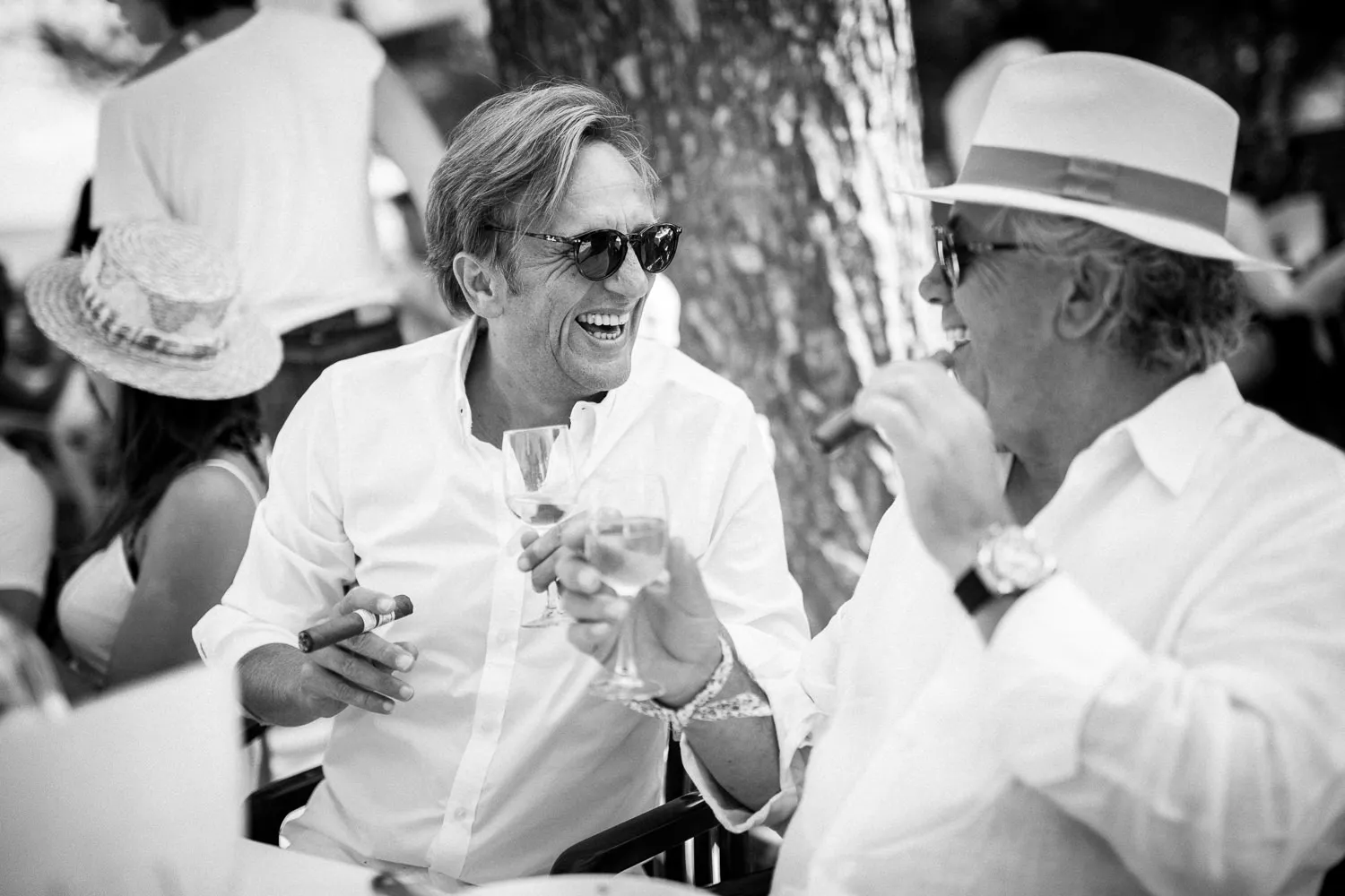 Black and white candid photo of two male guests laughing, enjoying drinks/cigars at a Geneva wedding - wedding photographer Geneva guest moments