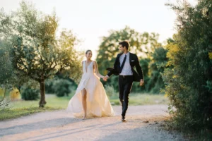 A happy bride and groom walk hand-in-hand through a sunlit olive grove, a candid moment captured by their wedding photographer in Spain.