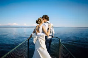 A stylish bride and groom kiss on the bow of a boat on Lake Geneva, a stunning portrait by their wedding photographer in Lausanne.