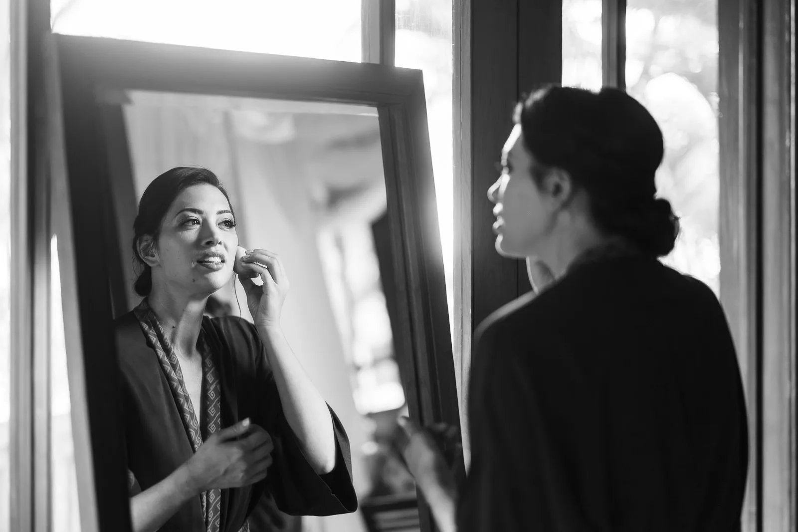 Black and white photo of bride applying makeup while looking in a mirror before her Lombok wedding - captured by wedding photographer Lombok.