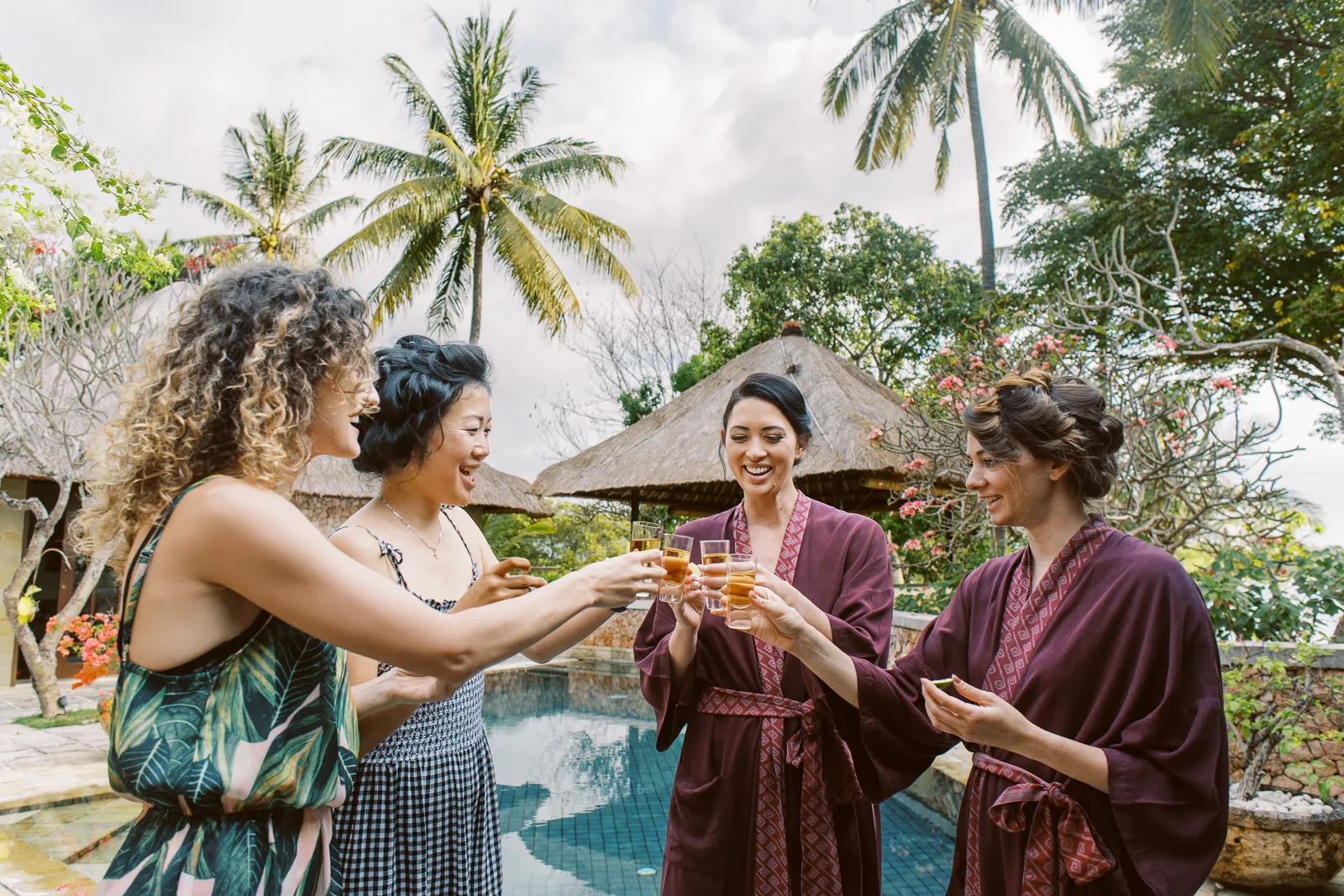Bride and friends laughing and toasting with drinks by the pool at a Lombok villa - captured by wedding photographer Lombok.