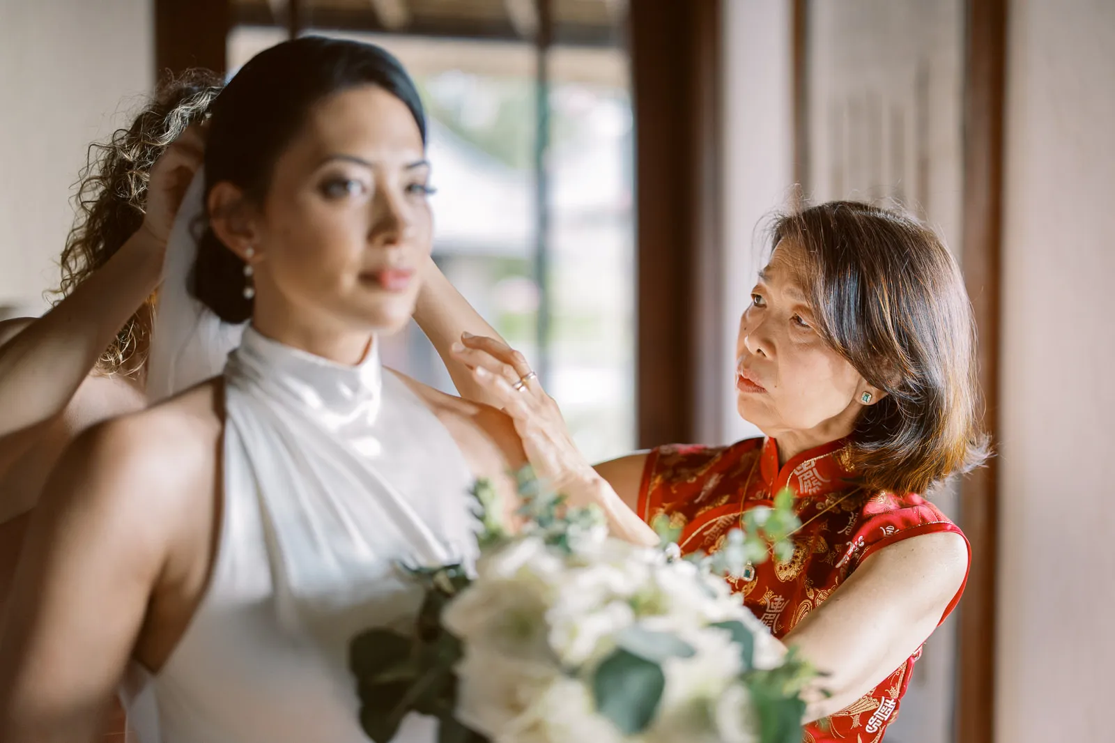 Mother in traditional red dress adjusting bride's veil before Lombok wedding ceremony - moment captured by wedding photographer Lombok.