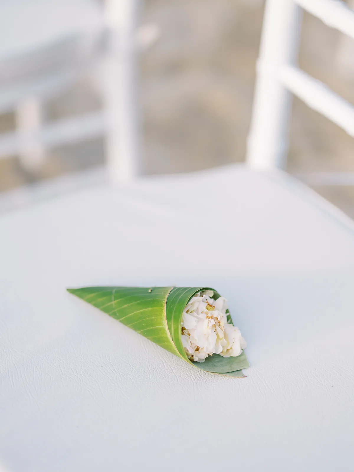 Single green leaf cone filled with white flower petal confetti on a white chair at Lombok wedding - detail by wedding photographer Lombok.