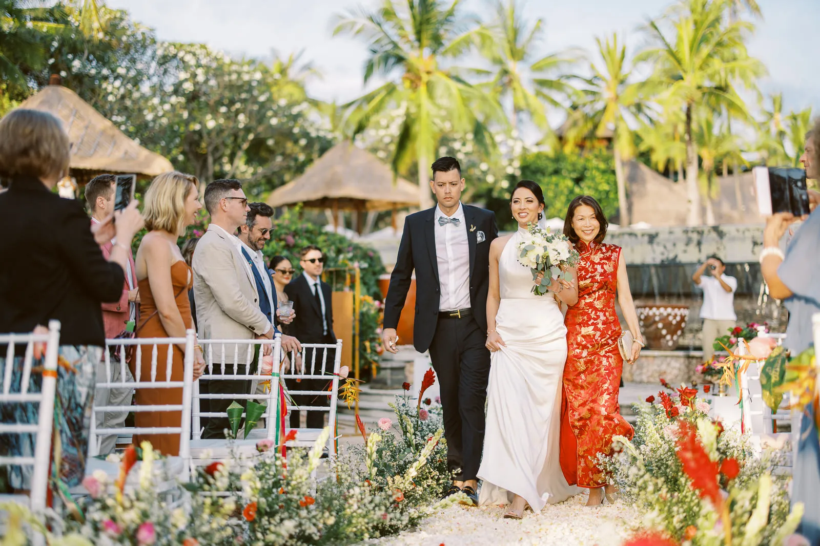 Bride in white halter dress walking down the aisle with her mother in traditional red dress at Lombok wedding - photo by wedding photographer Lombok.
