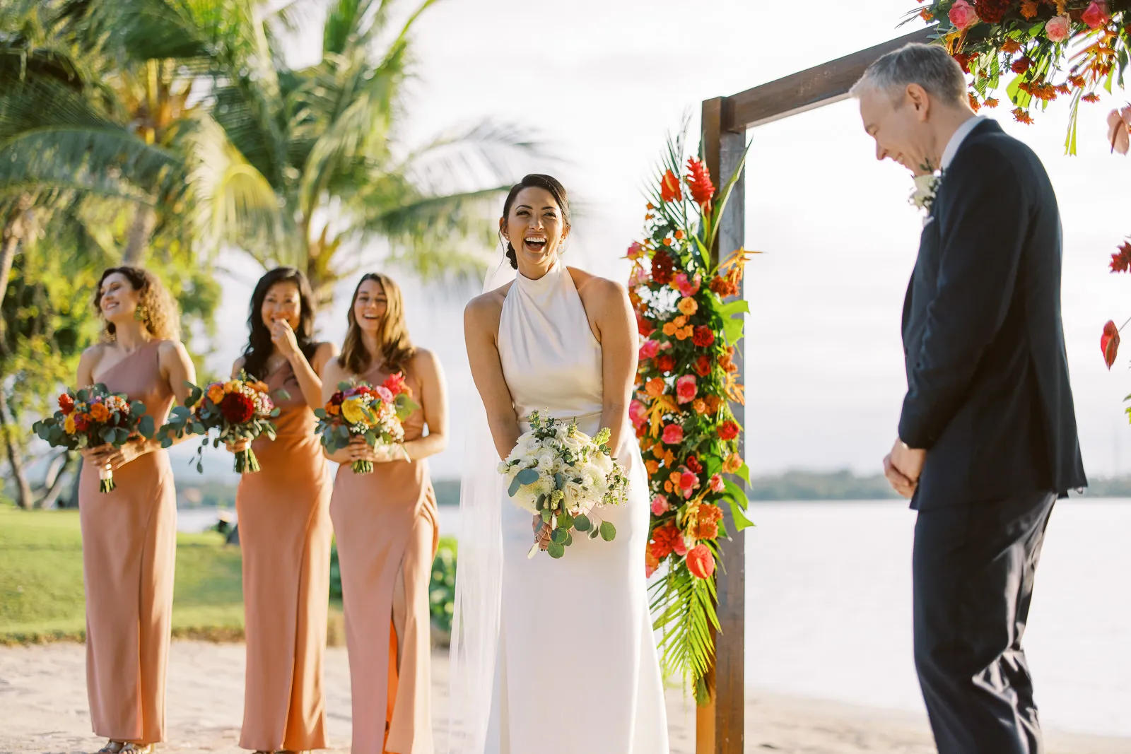 Bride laughing joyfully during her beach wedding ceremony in Lombok, bridesmaids behind - photo by wedding photographer Lombok.