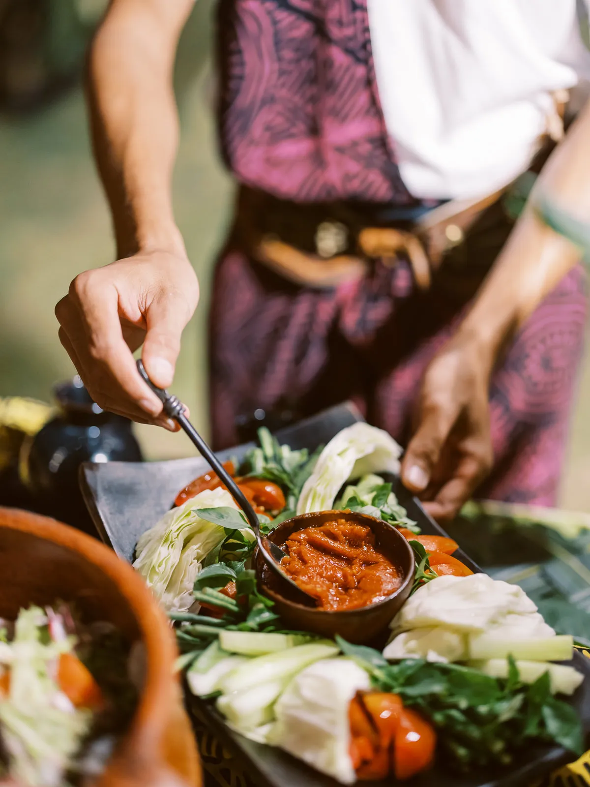 Server in traditional Lombok attire serving fresh salad with sambal - food photo by wedding photographer Lombok.
