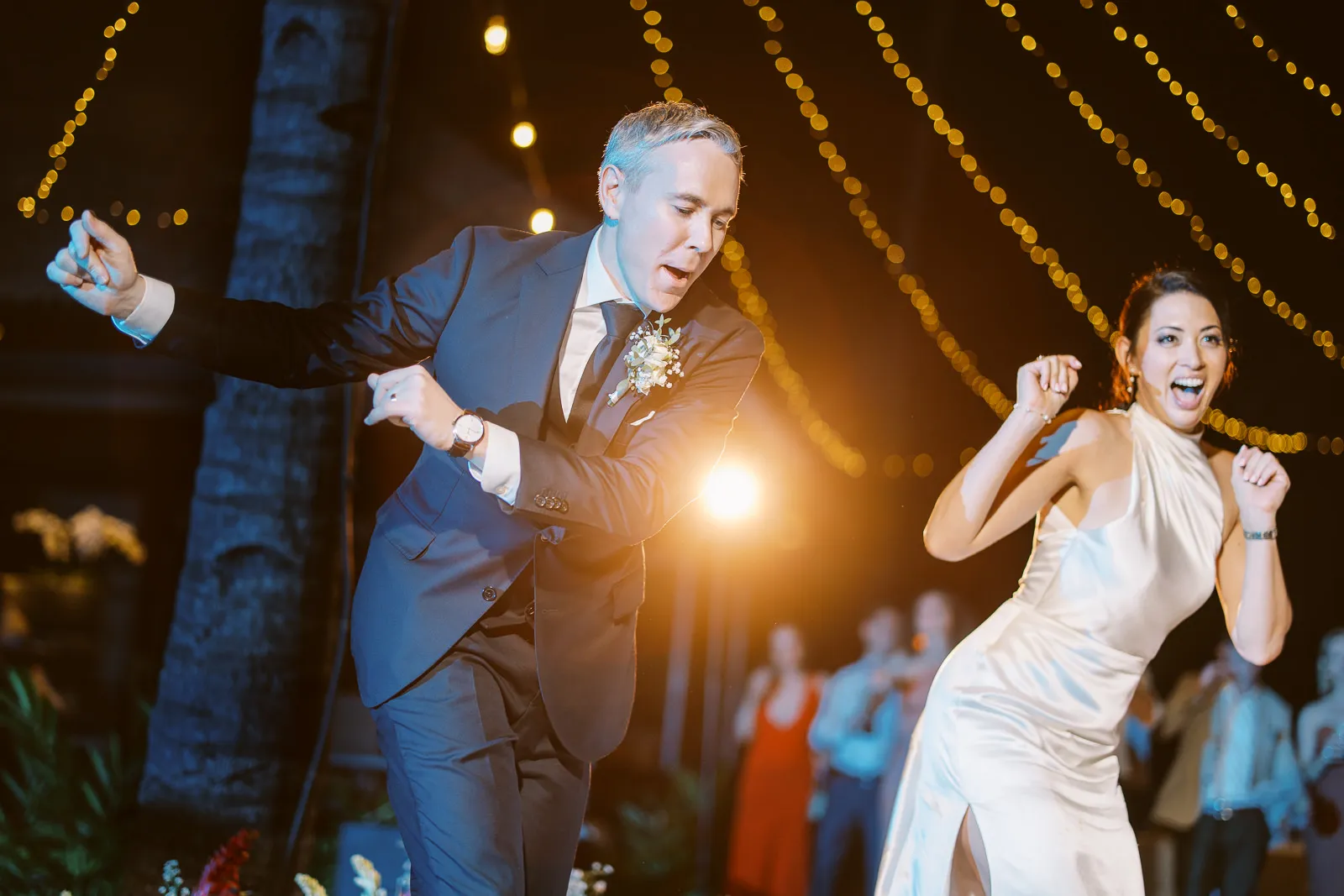 Bride and groom dancing energetically under string lights at their Lombok wedding party - photo by wedding photographer Lombok.