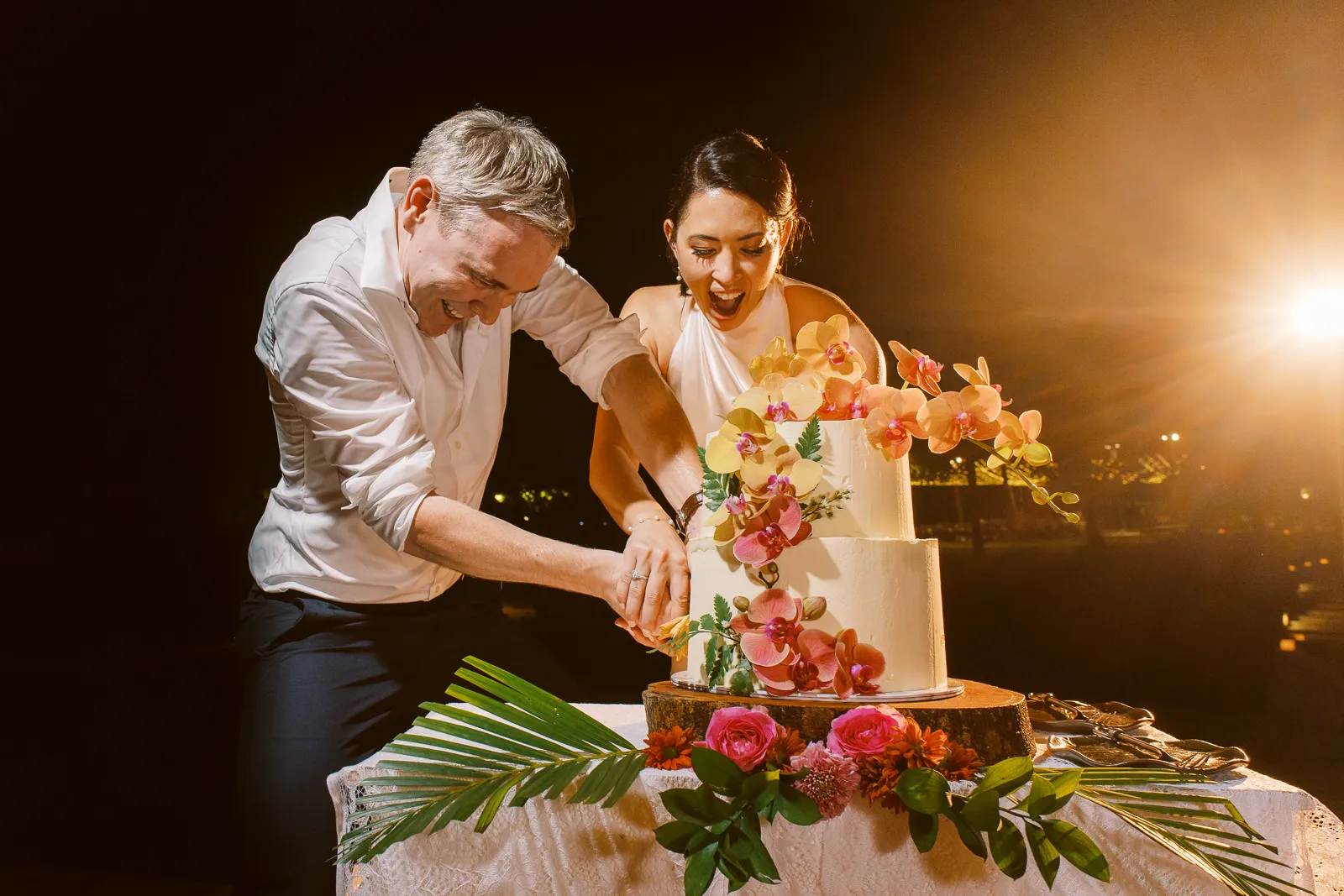 Bride and groom laughing while cutting their orchid wedding cake together in Lombok - photo by wedding photographer Lombok.