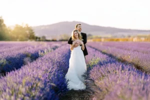 A happy couple in a vast purple lavender field, the groom embraces the bride from behind as they both smile, a romantic photo captured by a wedding photographer in Provence.