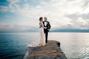 A bride and groom stand together on a stone pier against a dramatic sky, in an epic photo by a wedding photographer in Saint Tropez.