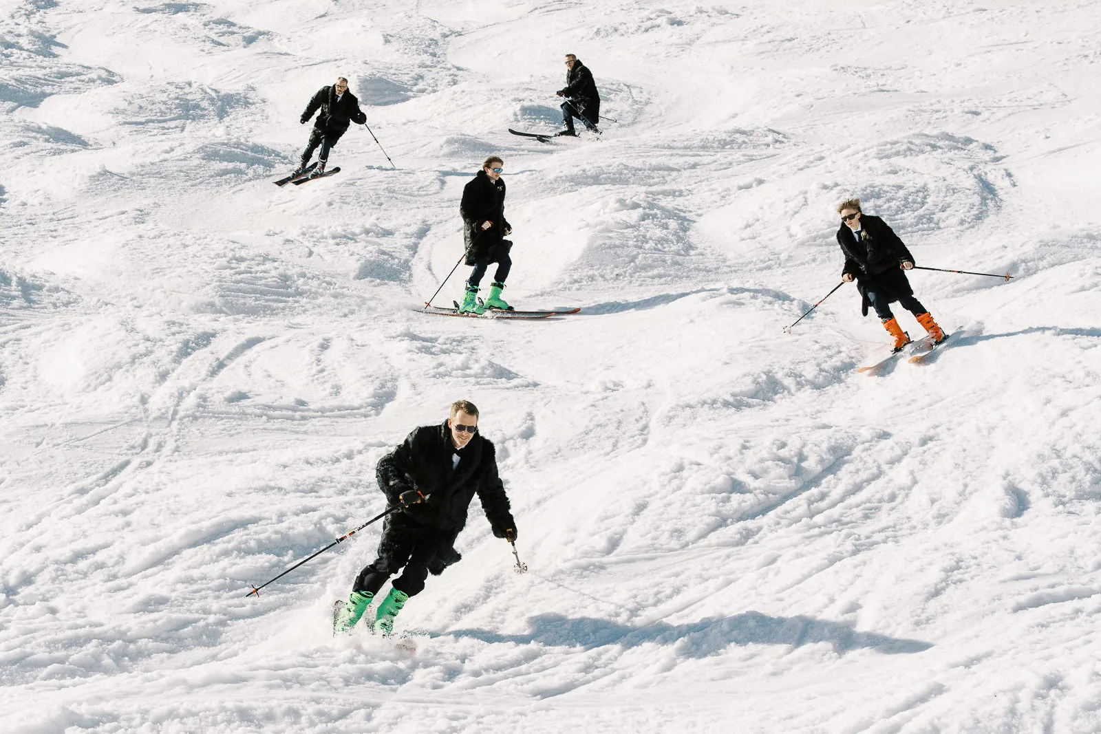 Wedding guests dressed in suits skiing down a sunny slope, a fun action shot from a winter wedding in Megeve, French Alps.