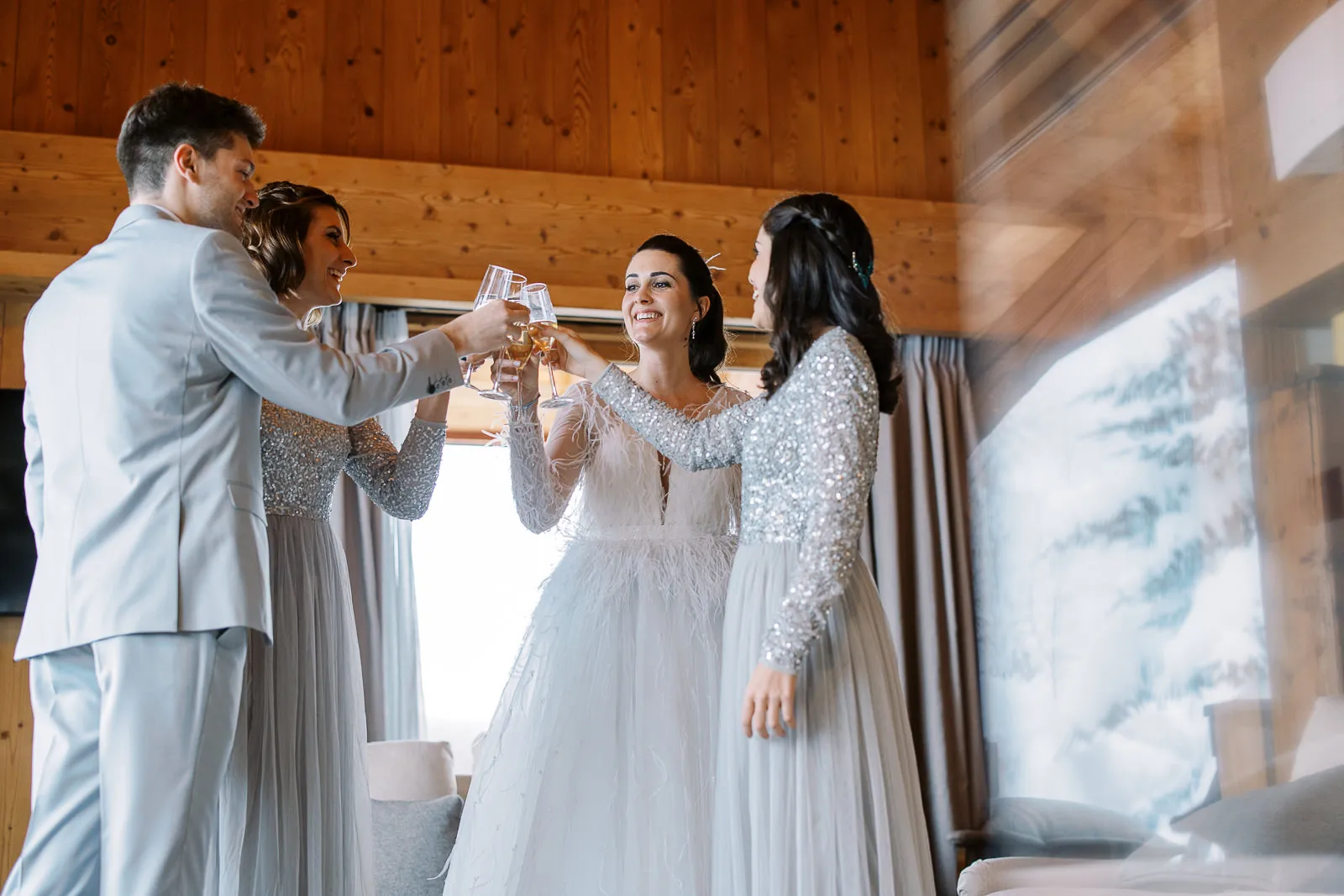 A bride and her wedding party share a champagne toast in a cozy wood-paneled room, captured by their Megeve wedding photographer.