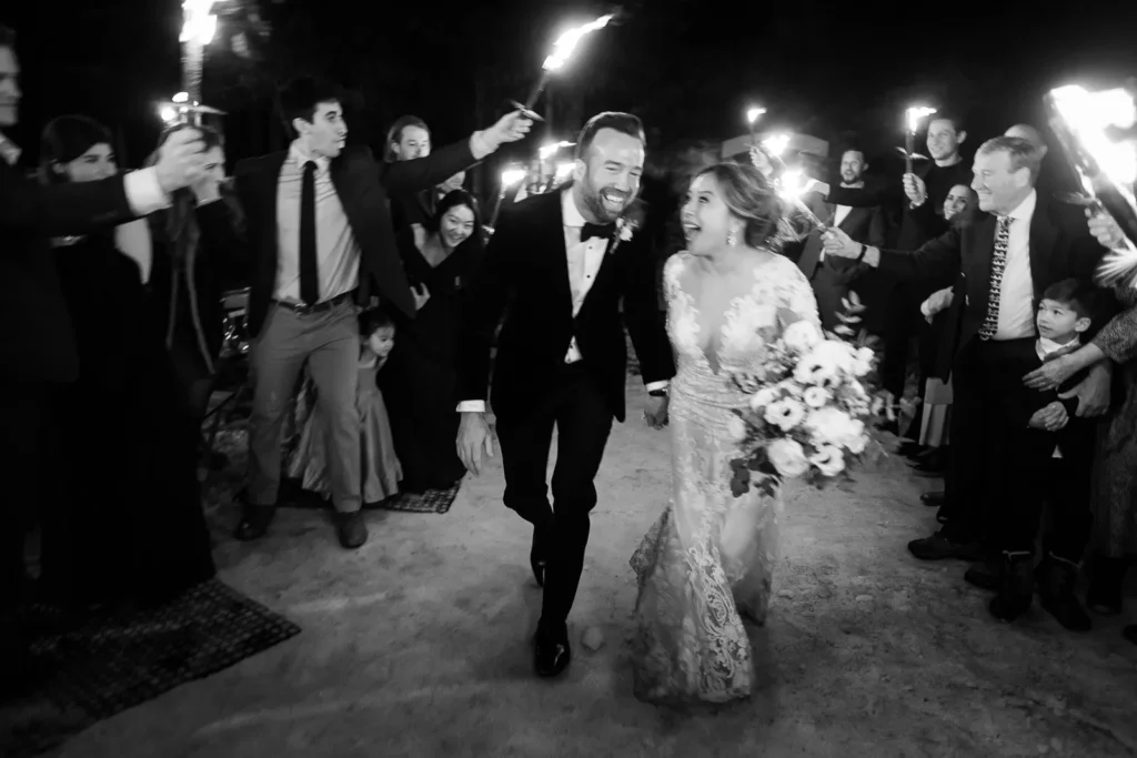 A joyful black and white photo of a couple's grand exit through guests holding torches at their Megeve wedding reception.