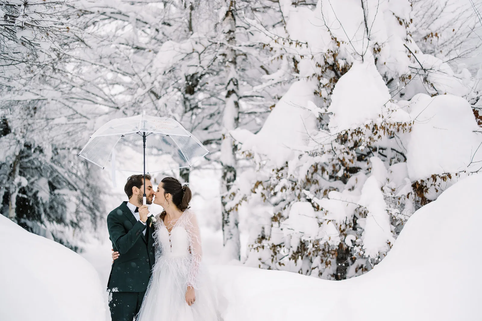 An intimate portrait of a bride and groom kissing under a clear umbrella in a snow-covered forest in Megeve, French Alps.