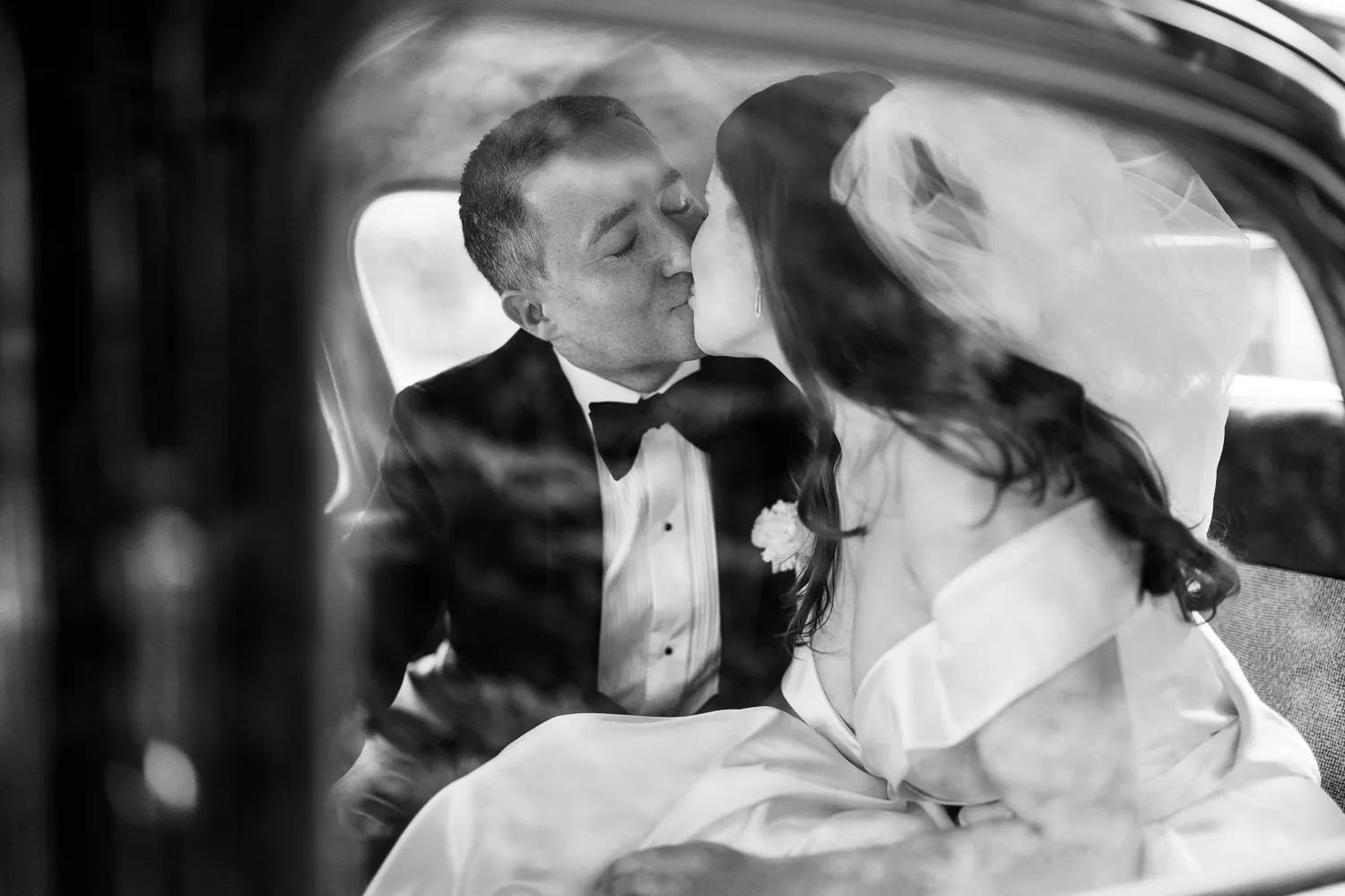 Black and white photo of bride and groom kissing in the back of a vintage car in Paris - by Wedding photographer Ritz Paris.