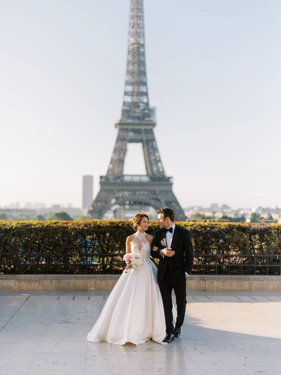 Bride and groom walking arm-in-arm with the Eiffel Tower in the background in Paris - photo by Wedding photographer Ritz Paris.