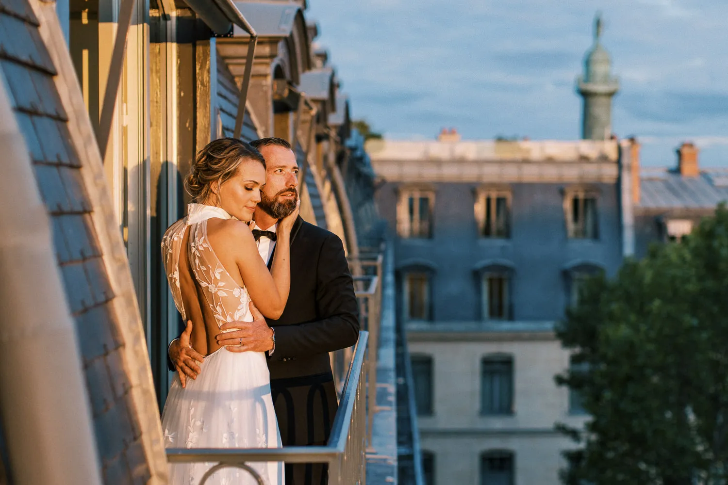 Elegant bride and groom embracing on a Parisian balcony at sunset, overlooking rooftops - photo by wedding photographer Ritz Paris.