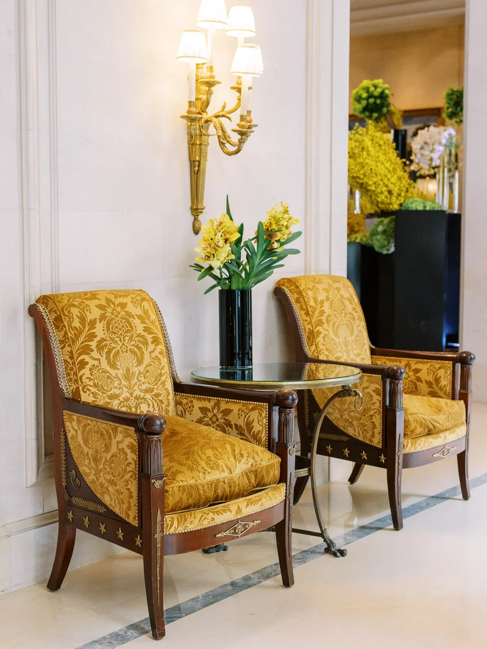 Two elegant, antique-style chairs with gold brocade upholstery in a luxurious Parisian hotel lobby.