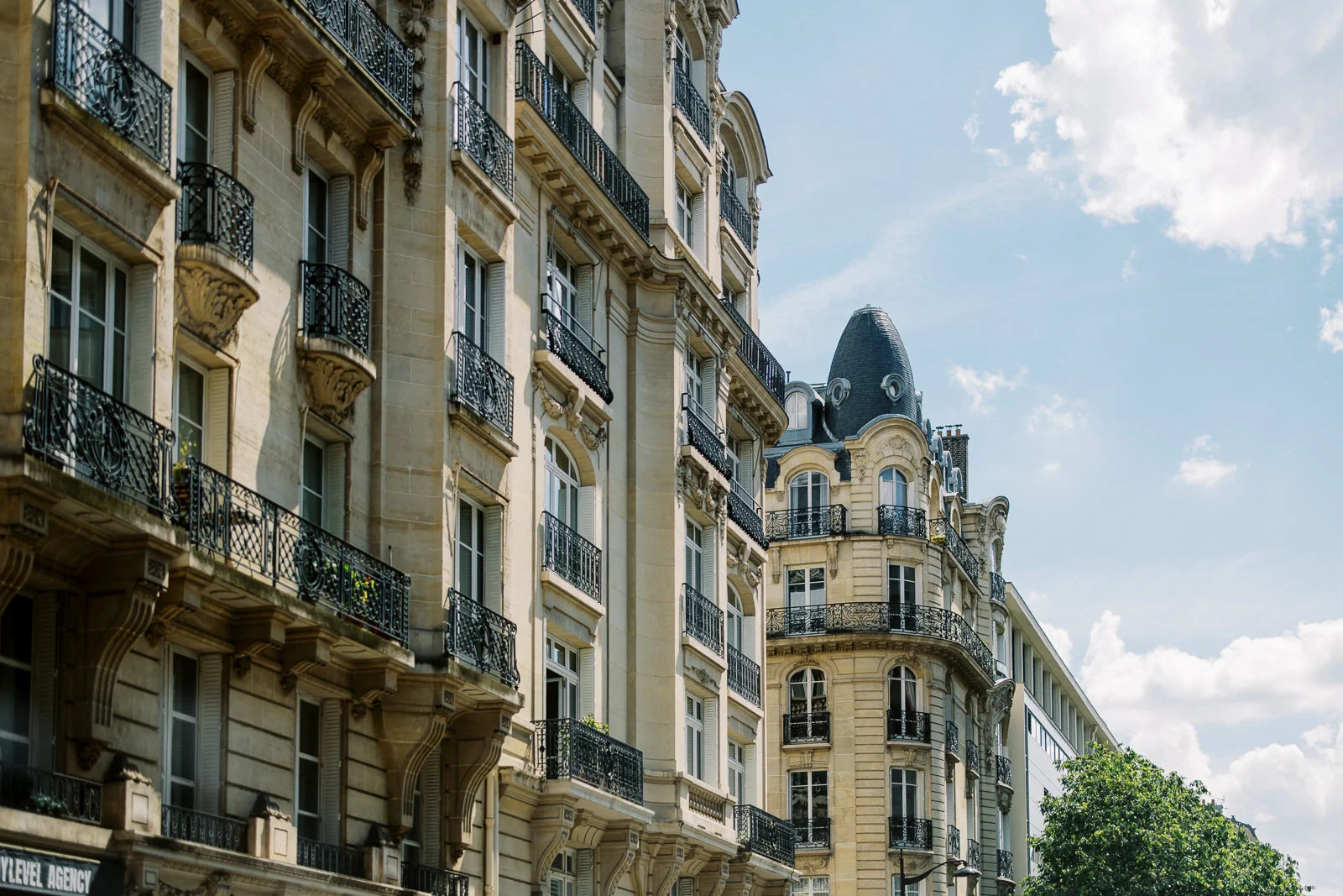 Classic Parisian Haussmann architecture with ornate iron balconies under a blue sky with fluffy clouds. How Much Does a Photographer in Paris Cost?