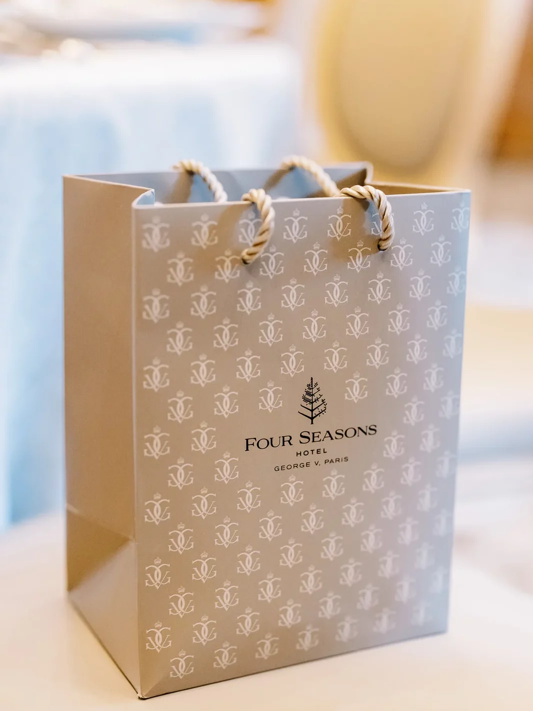 A chic, gray gift bag from the luxury Four Seasons Hotel George V, Paris, sitting on a table. How Much Does a Photographer in Paris Cost?