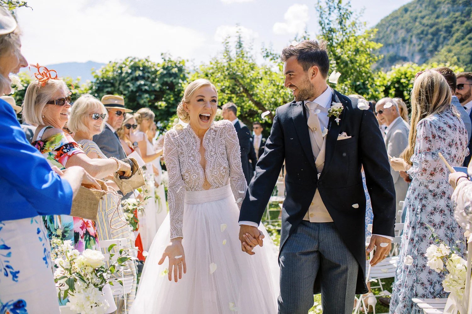 Smiling bride and groom walk through showering petals, captured by a Wedding photographer Lake Como. Photographe Mariage Lac de Côme.