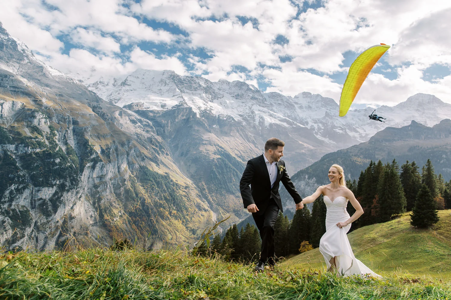 Bride and groom running in the Swiss Alps captured by a Davos wedding photographer with a paraglider.