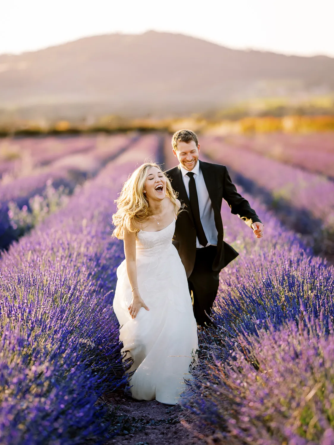 Joyful couple laughing and running through a vibrant lavender field, captured by a wedding photographer About Sylvain Bouzat.
