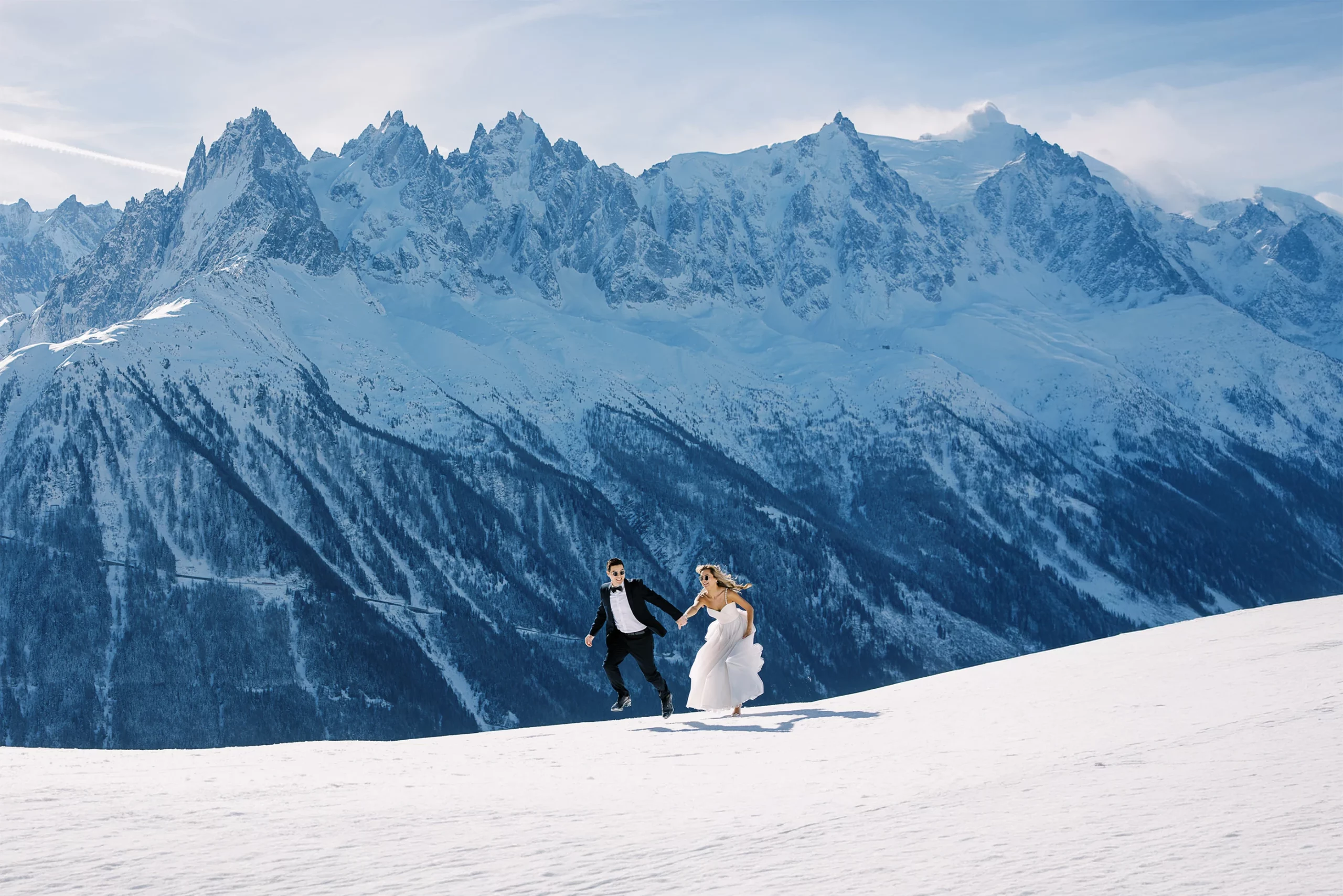 Joyful couple runs hand-in-hand on a pristine snowy mountain, captured by a Wedding photographer Crans-Montana.