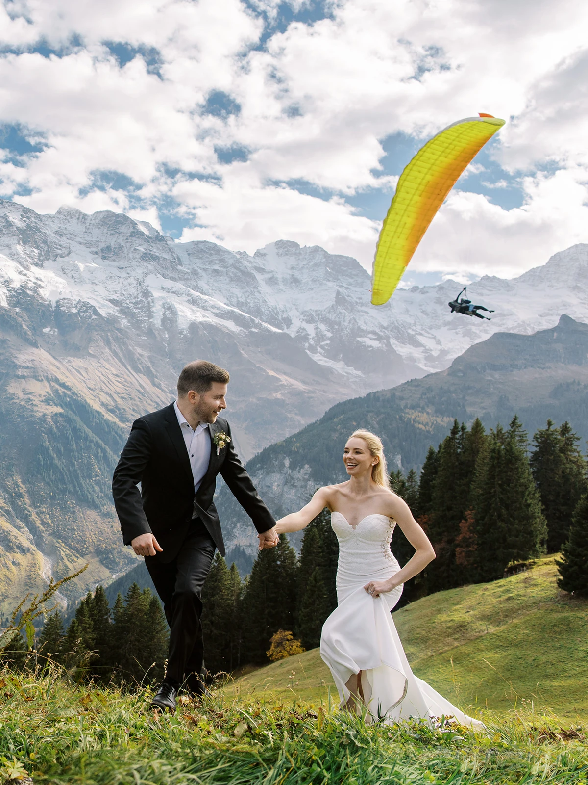 Joyful couple on mountain slope with paraglider, captured by wedding photographer Crans-Montana.