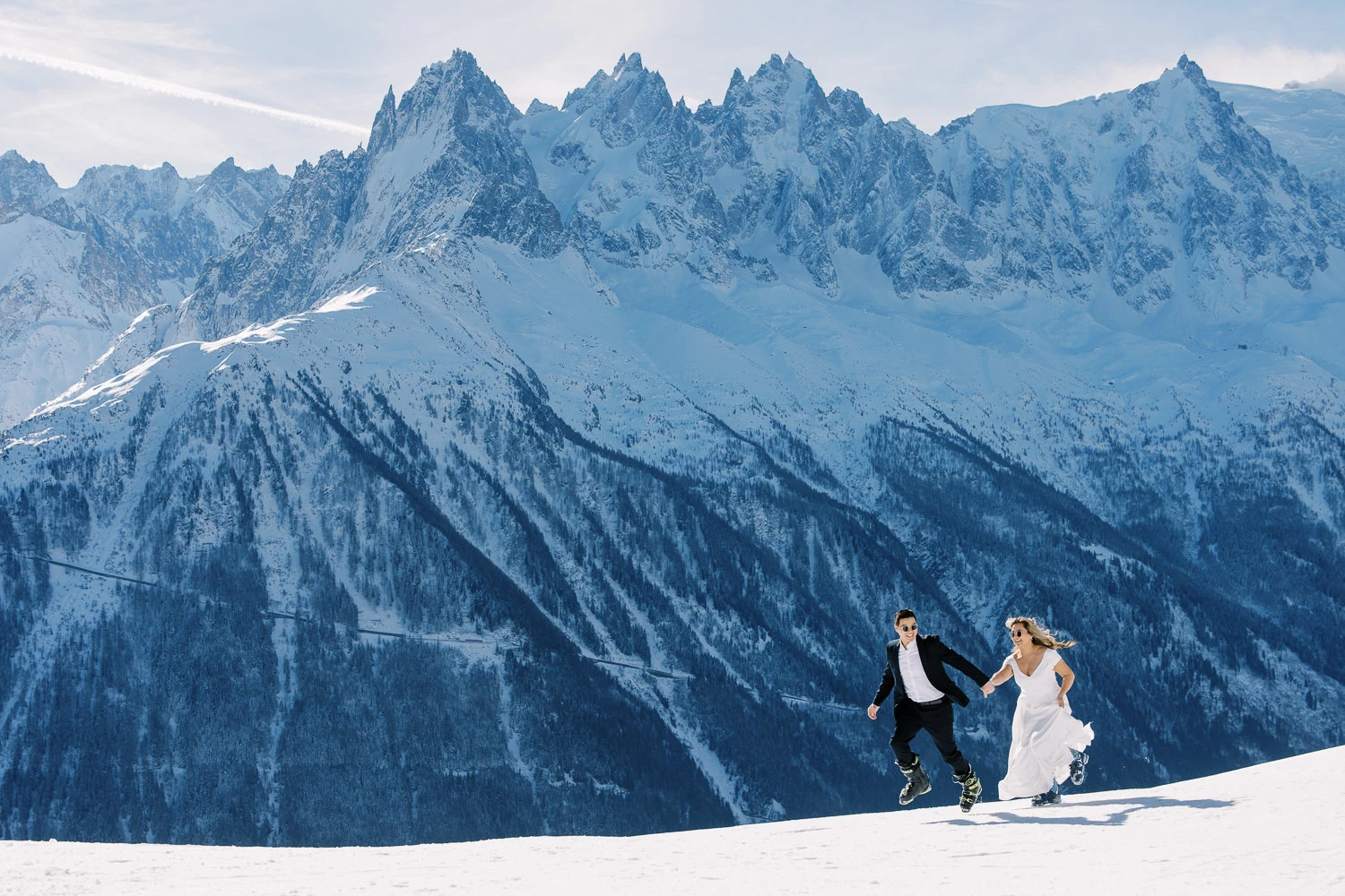 Joyful couple in wedding attire runs through fresh snow, captured by a Wedding photographer French Alps.