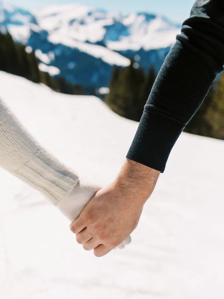 Un couple se tenant la main dans les montagnes enneigées par un photographe de mariage.