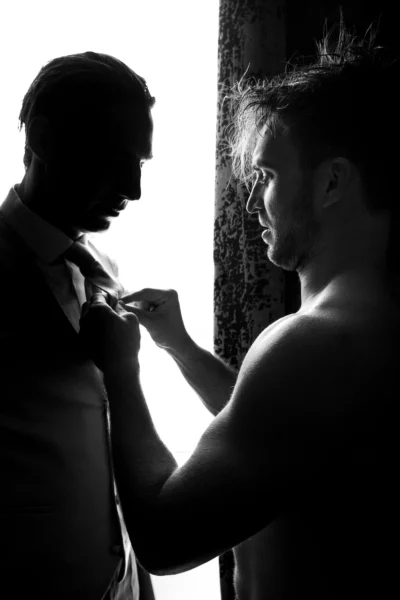 Silhouette of groom prep by a French wedding photographer in a luxury hotel suite.