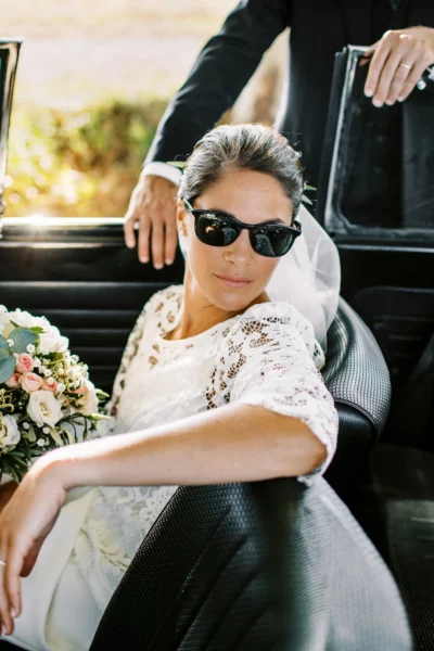 Bride wearing sunglasses in a vintage car by a french wedding photographer.