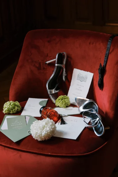 Silver heels and wedding stationery on a red velvet chair by a French wedding photographer.