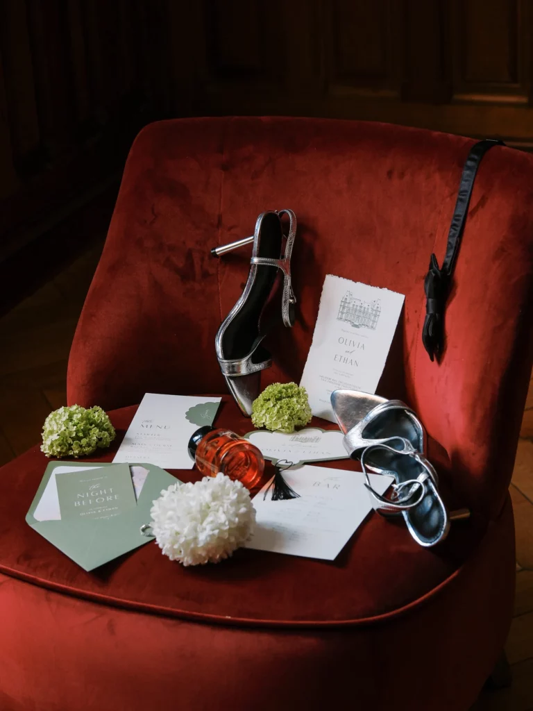 Silver heels and wedding stationery on a red velvet chair by a French wedding photographer.