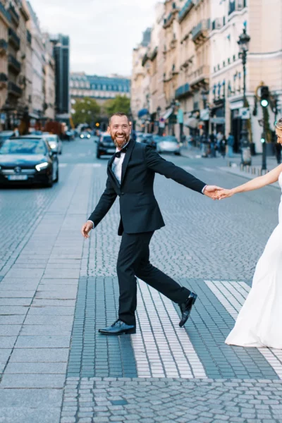 A joyful bride and groom crossing a Parisian street by a French wedding photographer.