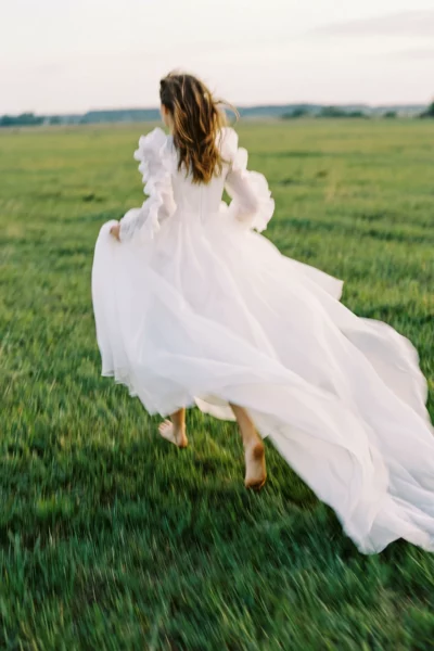 A barefoot bride running through a lush meadow, captured by a french wedding photographer.