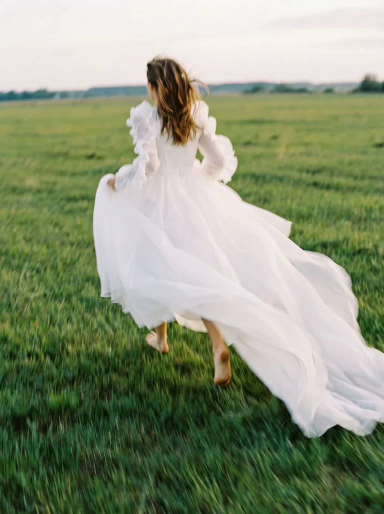 A barefoot bride running through a lush meadow, captured by a french wedding photographer wedding photographer.