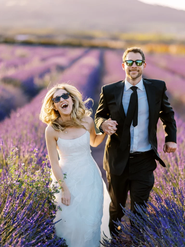 Bride and groom wearing sunglasses running through lavender fields by a French wedding photographer.