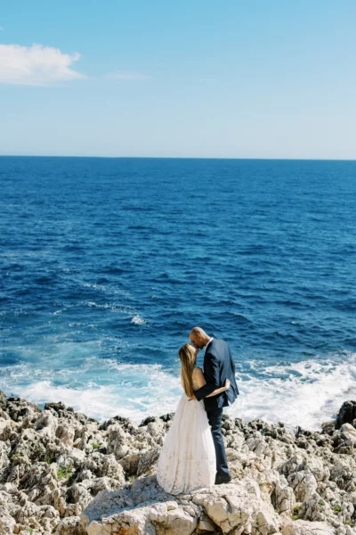 Bride and groom kissing on rocky cliffs by the sea, captured by a French wedding photographer.