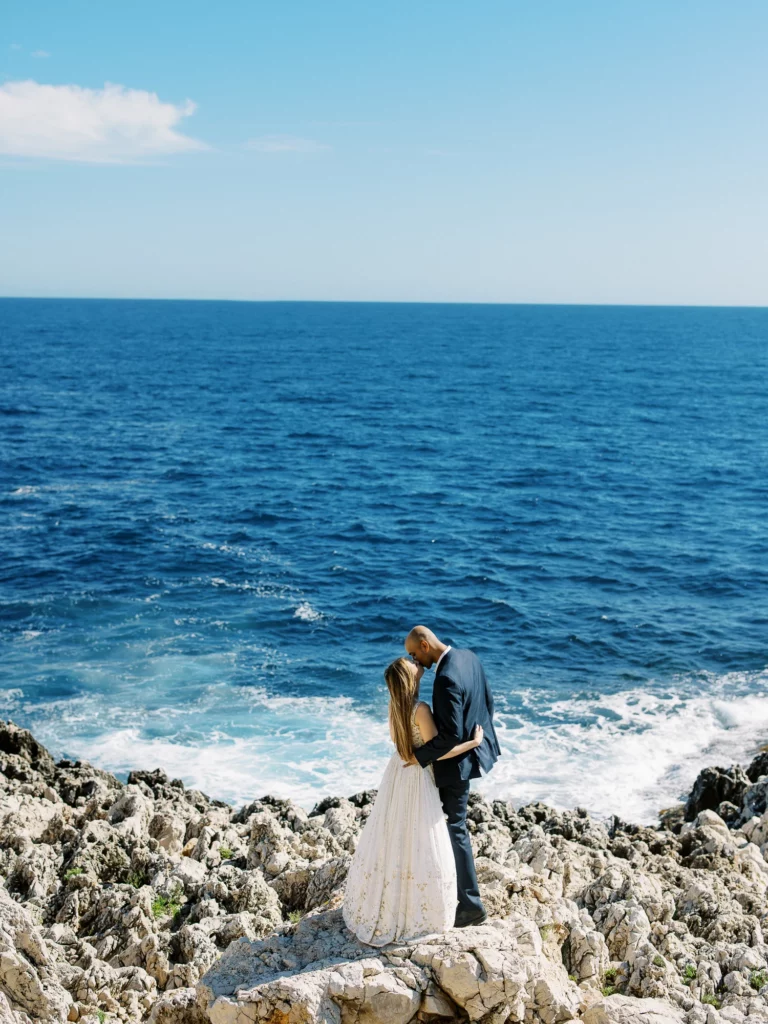 Bride and groom kissing on rocky cliffs by the sea, captured by a French wedding photographer.